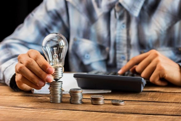 Persona calculando el precio de la electricidad con monedas y bombilla
